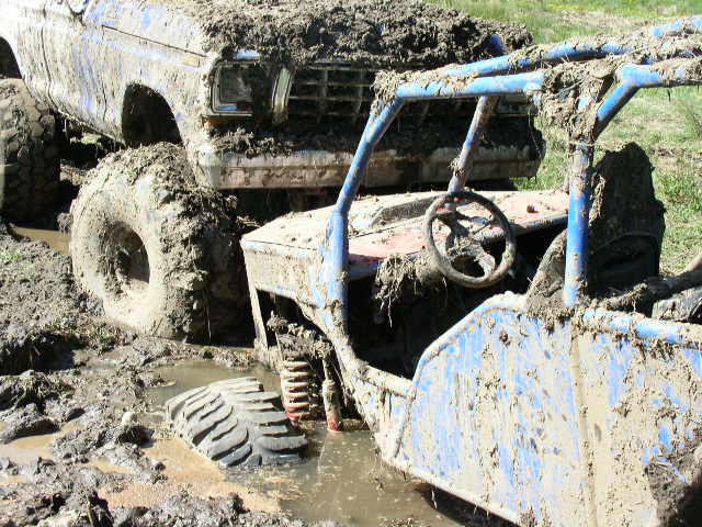 Mud-covered blue Ford Bronco stuck in mud next to a blue off-road buggy.