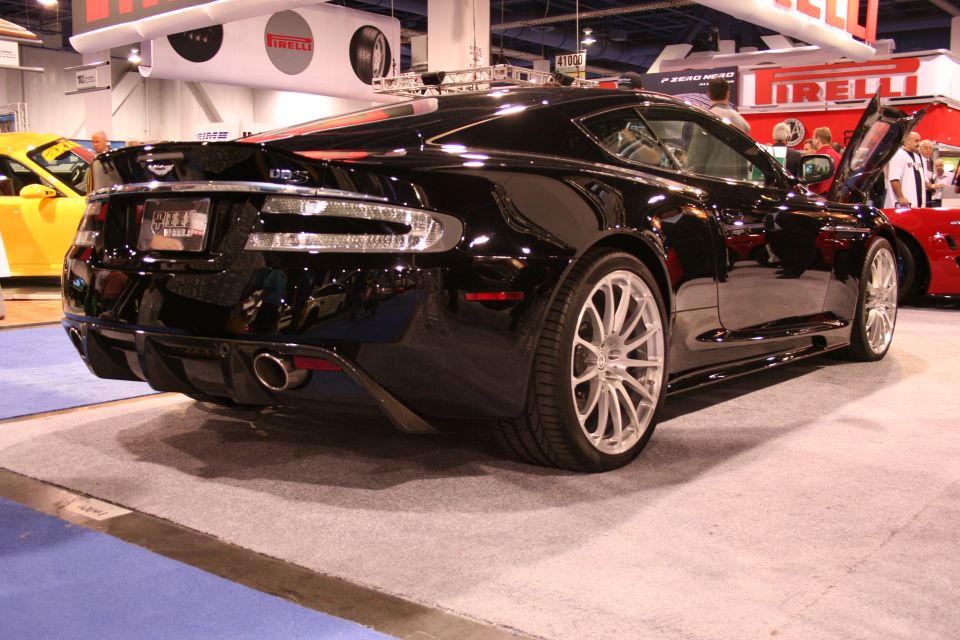 Black Aston Martin coupe rear three-quarter view at a Pirelli auto show booth