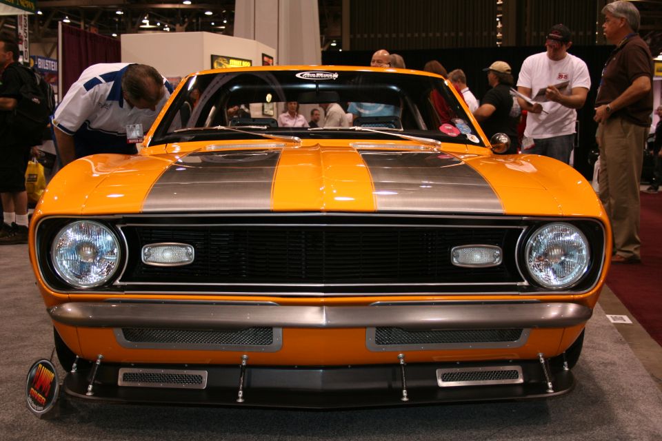 Front view of an orange classic car with silver racing stripes and a black grille