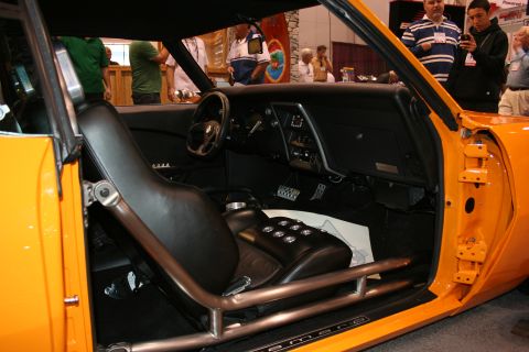 Interior of an orange muscle car with black racing seats and a roll cage. Dashboard and steering wheel visible