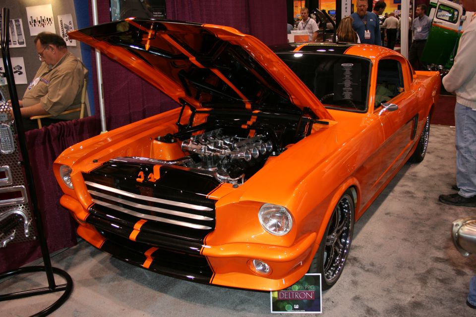Orange and black customized classic car with hood open showing engine. Displayed indoors