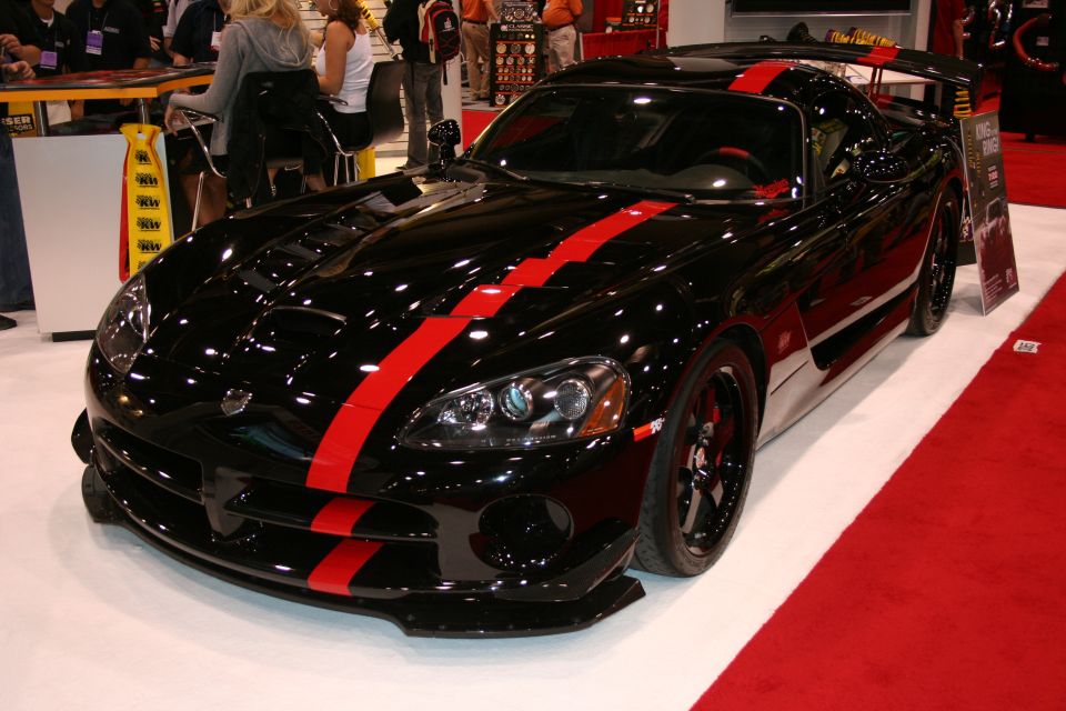 Black Dodge Viper with red racing stripes, front 3/4 view, on display with red carpet