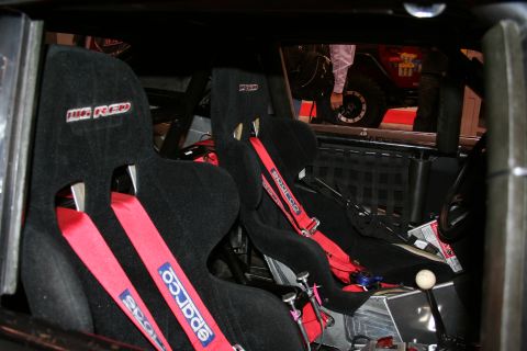 Two black Sparco racing bucket seats with red harness belts inside a caged car
