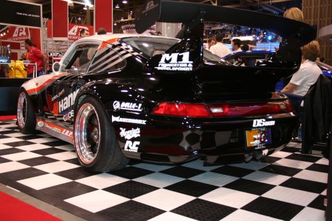 Black Porsche 911 race car with rear wing at an auto show, rear quarter view
