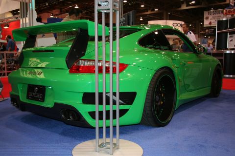 Green Porsche 911 with a large rear spoiler and black wheels, viewed from the rear