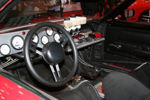Custom racing car interior showing a large steering wheel, multiple gauges, and brake fluid reservoirs