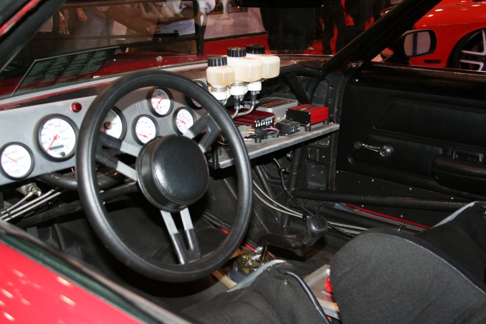 Custom racing car interior showing a large steering wheel, multiple gauges, and brake fluid reservoirs