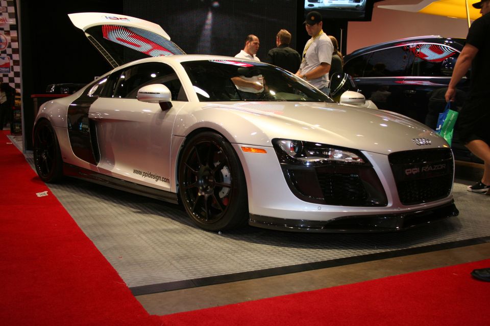 Silver Audi R8 sports car with butterfly doors open, parked on a red carpet. Text on the grille reads 'R8 RAZOR'