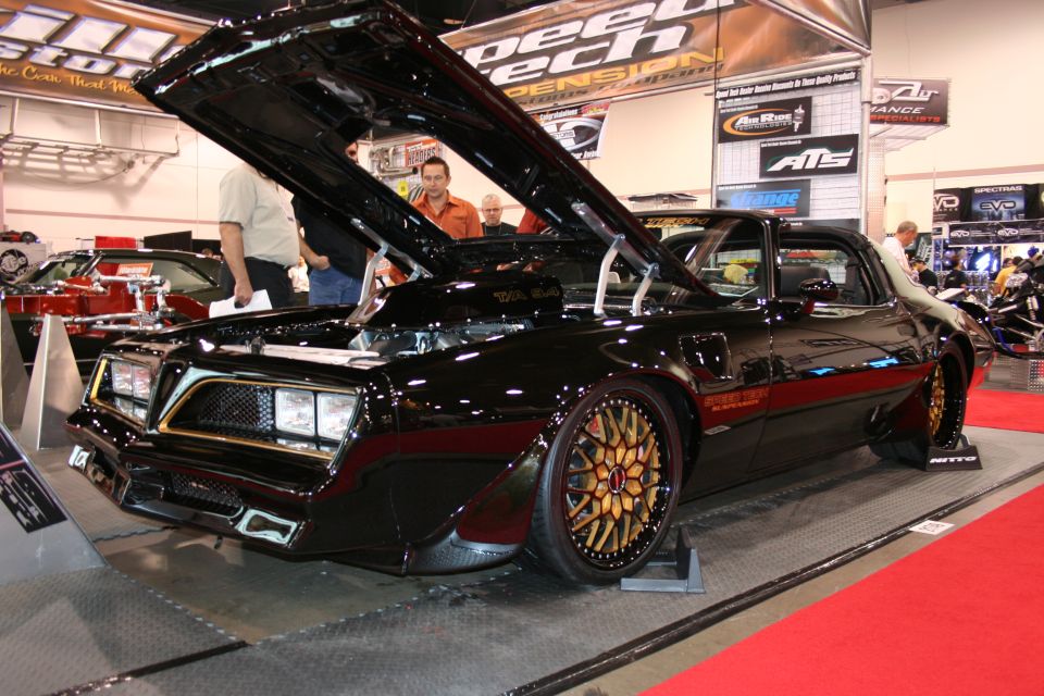 Black custom car with hood open, gold wheels, and red interior visible
