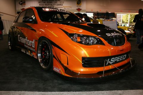 Orange Subaru WRX STI with black racing stripes and widebody kit, front 3/4 view