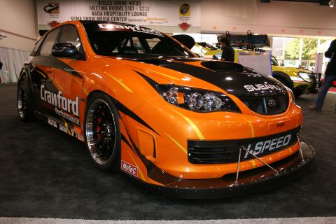 Orange Subaru WRX STI with black racing stripes, widebody kit, and 'X-SPEED' on front bumper
