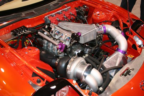 Engine bay with a large turbocharger, intercooler, and custom intake piping. Red engine covers and orange body