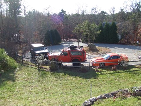 1995 Ford Mustang - An orange coupe, a red SUV with a roof rack, and a black SUV are parked in a residential driveway.