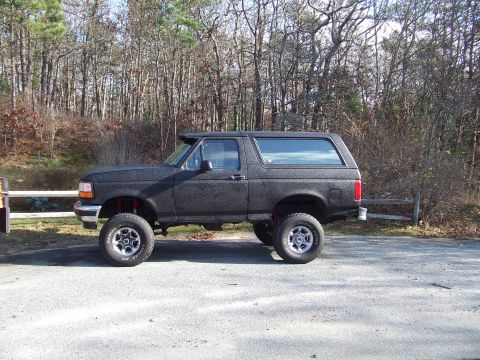 1995 Ford Mustang - Lifted black Ford Bronco from the mid-1990s is shown from the side.