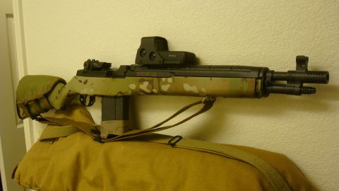 1990 Ford Bronco - A rifle with a camouflage pattern and tactical accessories is displayed against a wall.