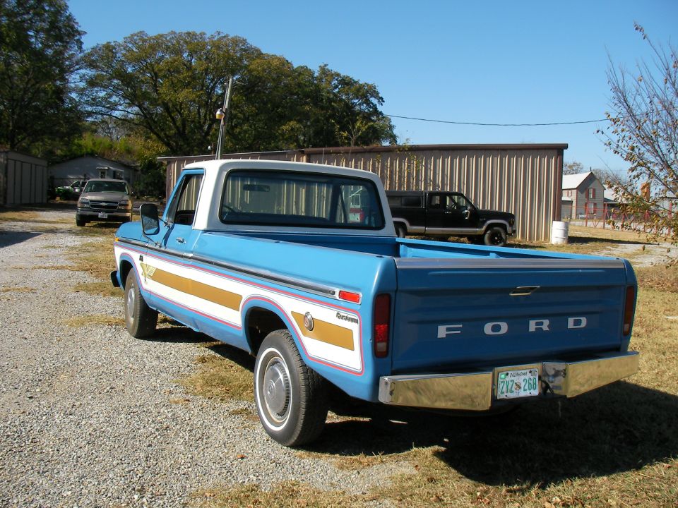 Blue 1976 Ford F-150 pickup truck parked outside with a silver pickup and a black SUV in the background