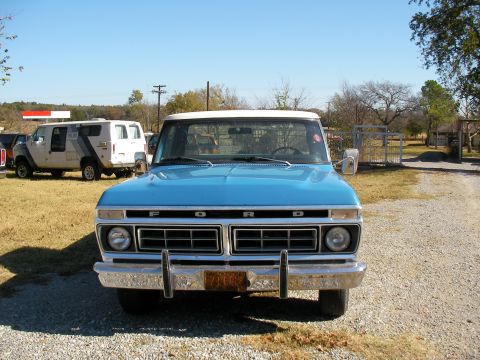 1976 Ford F-150 - A blue 1973 Ford F-150 truck is parked on a gravel driveway with a white van in the background.