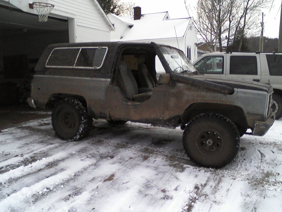 Muddy two-tone lifted GM Blazer-style SUV with doors removed parked on snowy driveway
