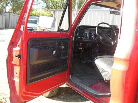 1979 Ford F-350 - Interior view of a red 1979 Ford F-350 pickup truck, showing the dashboard and driver's seat with the door ajar.