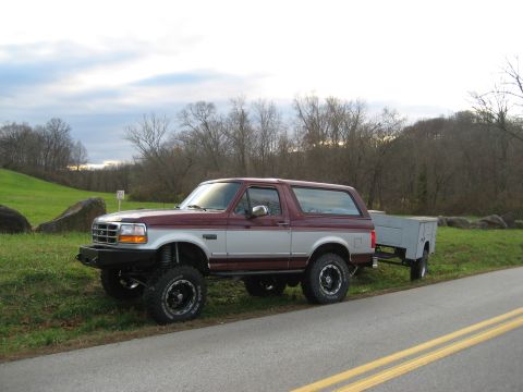 1996 Ford Bronco - A lifted 1996 Ford Bronco is parked on the side of the road, hitched to a small utility trailer.