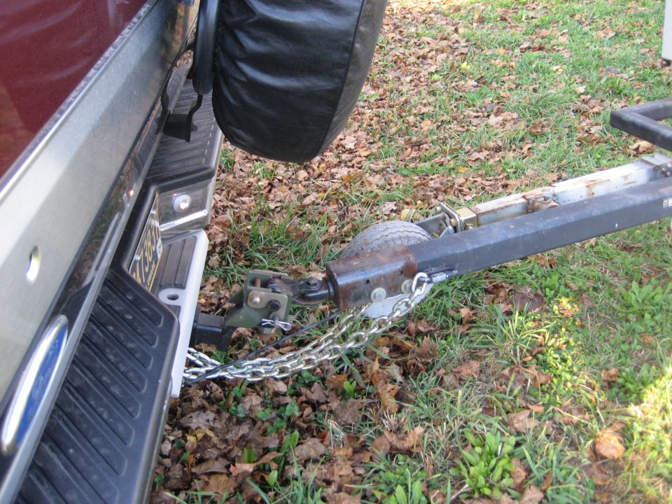 Trailer hitch and safety chains attached to the rear bumper of a dark red vehicle