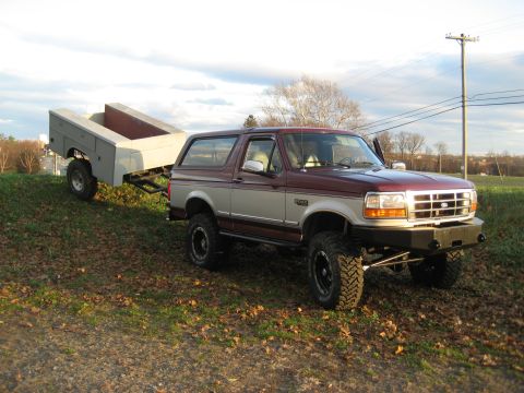 1996 Ford Bronco - A lifted 1996 Ford Bronco tows a utility trailer on a grassy hill under a cloudy sky.