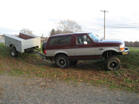 1996 Ford Bronco - A maroon and silver Ford Bronco is seen from the side, towing a utility trailer.
