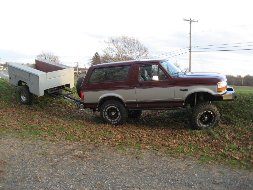Maroon and silver Ford Bronco towing a utility trailer