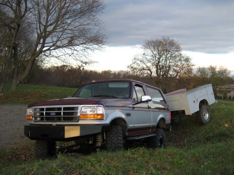 1996 Ford Bronco - The two-tone Ford Bronco is equipped with an aftermarket bumper and lifted suspension, towing a trailer with storage compartments.