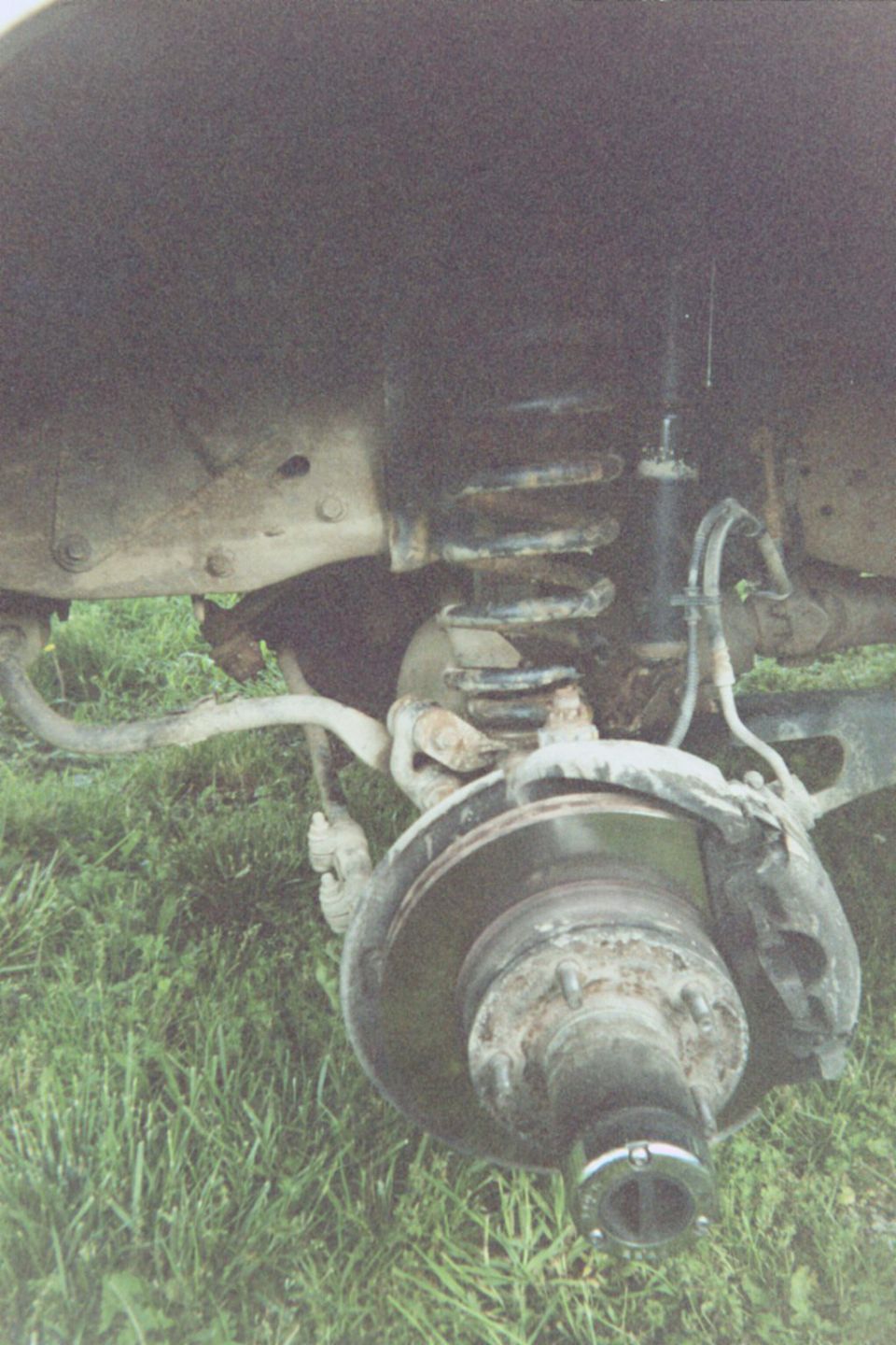 Front hub and brake rotor with wheel removed, coil spring and shock visible, vehicle over grass