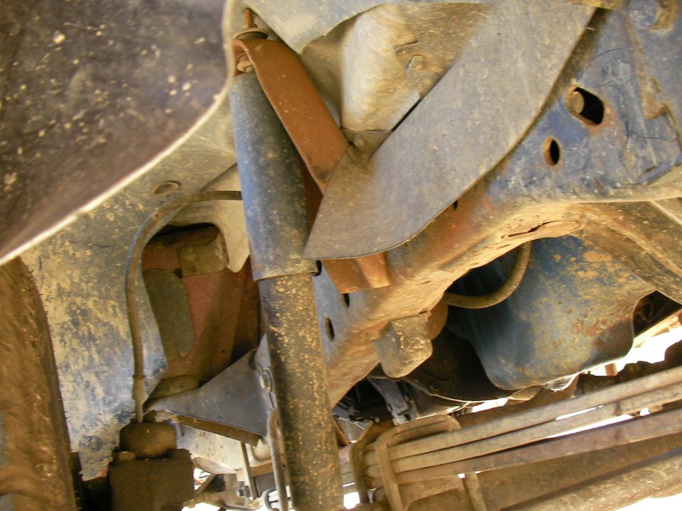 Underside view of a truck's suspension and frame, showing rust and wear