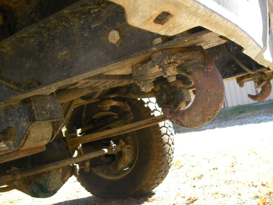Rusty tow hook attached to a vehicle's frame, showing suspension and tire