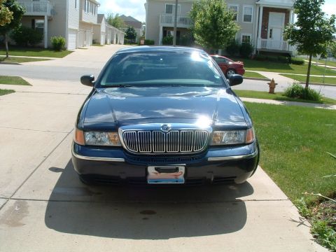 1999 Mercury Grand Marquis - A dark blue sedan is parked in front of a suburban house. The vehicle has a prominent chrome grille.
