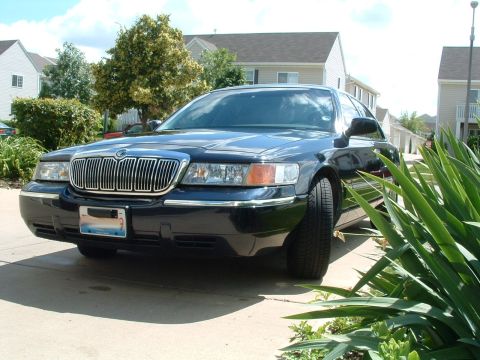 1999 Mercury Grand Marquis - A dark blue sedan with a prominent chrome grille is parked in a residential driveway.