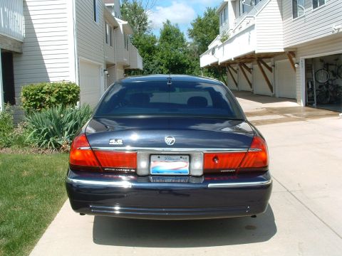 1999 Mercury Grand Marquis - Rear view of a dark blue sedan parked in a driveway with houses in the background.