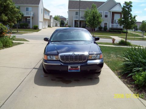 1999 Mercury Grand Marquis - A dark blue sedan is parked on a concrete driveway in front of a residential building.