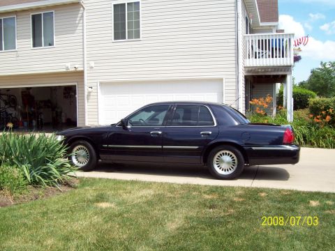 1999 Mercury Grand Marquis - A dark blue sedan is parked in a driveway next to a house with an open garage.