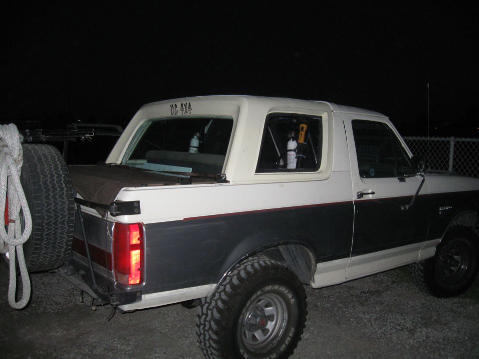 White and dark gray 1991 Ford Bronco with a spare tire mounted on the rear, seen at night