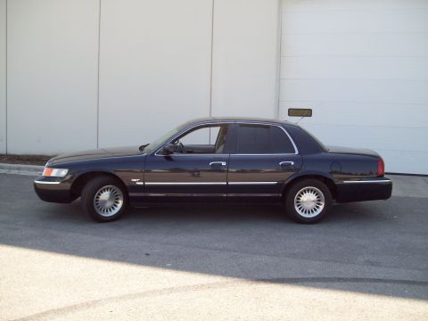 1999 Mercury Grand Marquis - A dark sedan is parked on asphalt in front of a large building with a garage door.