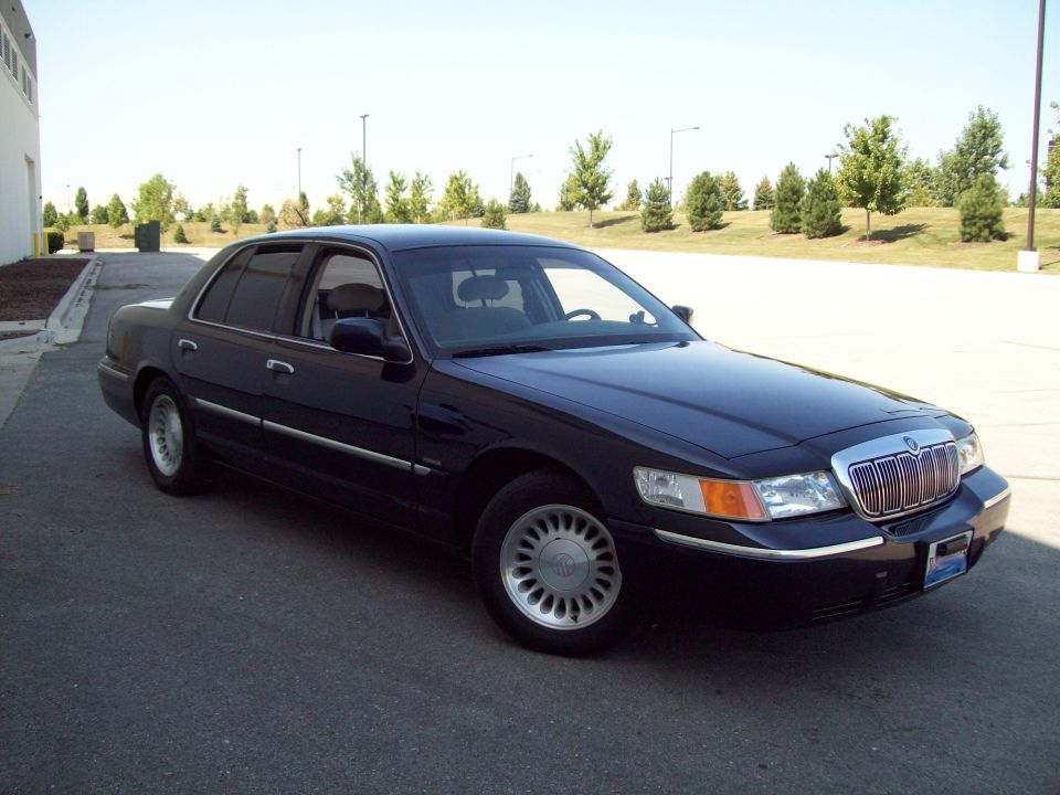 Dark sedan parked on asphalt, facing right. Chrome grille, headlights visible