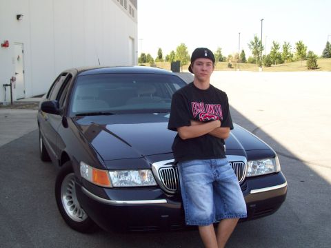 1999 Mercury Grand Marquis - A young man poses with a dark blue sedan in a parking lot.