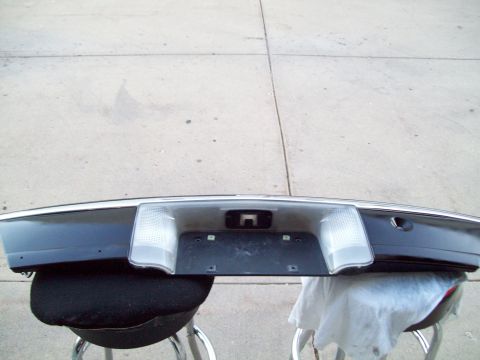 1999 Mercury Grand Marquis - A dark blue trunk lid finish panel with chrome trim removed from the car and laid across two stools on a concrete driveway. The rear licens…