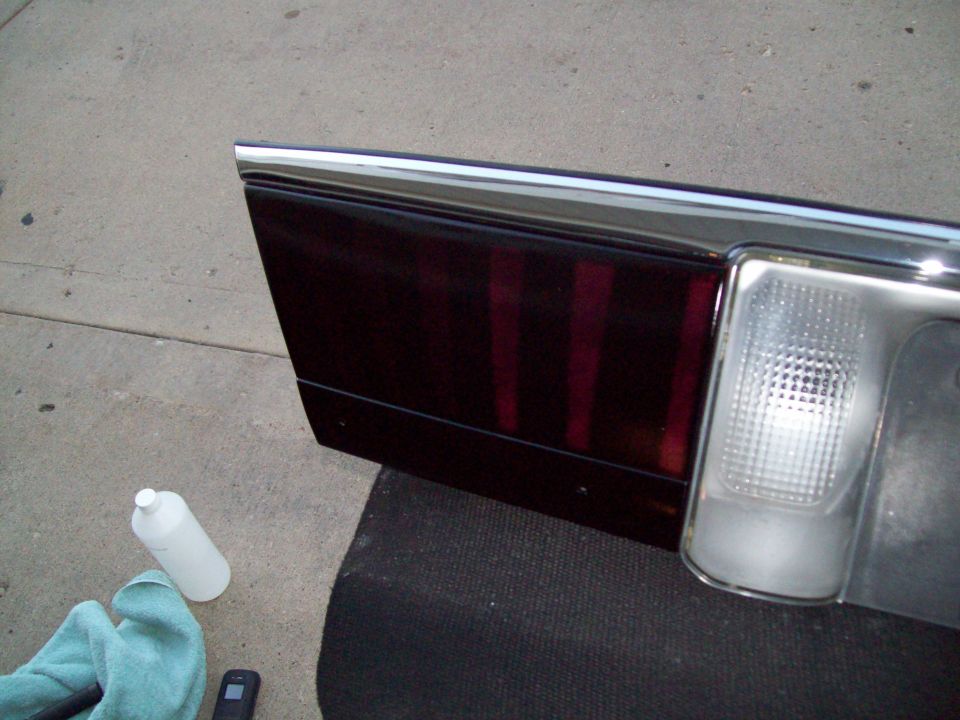 Car tail light assembly with dark red lenses and chrome trim, next to cleaning supplies
