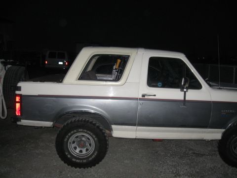 1991 Ford Bronco - A two-tone gray and white Ford Bronco is parked outdoors at night, with a spare tire visible on the back.