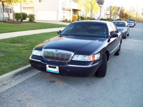 1999 Mercury Grand Marquis - A dark blue 1999 Mercury Grand Marquis is parked on a residential street with other vehicles behind it.