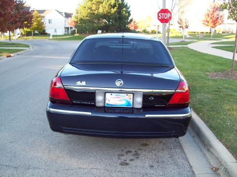 1999 Mercury Grand Marquis - Rear view of a Mercury Grand Marquis parked curbside on a street with houses and trees in the background.