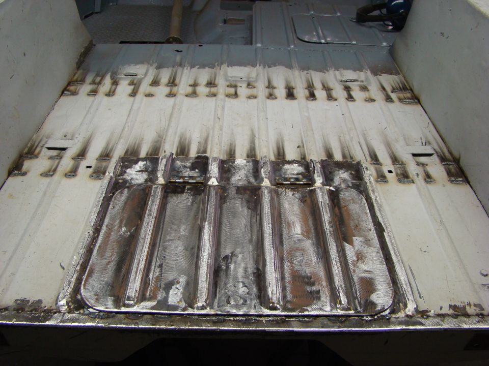 Interior floor of a vehicle undergoing repair, showing exposed metal and welding marks