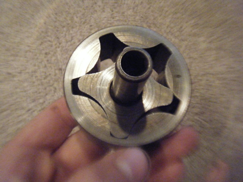 Hand holding a metal oil pump rotor with star-shaped internal vanes