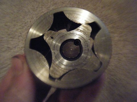 1979 Ford Bronco - A metal oil pump rotor is shown in a close-up view, held by a hand against a textured background.