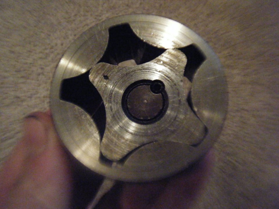 Close-up of a metal oil pump rotor with six lobes, held by a hand